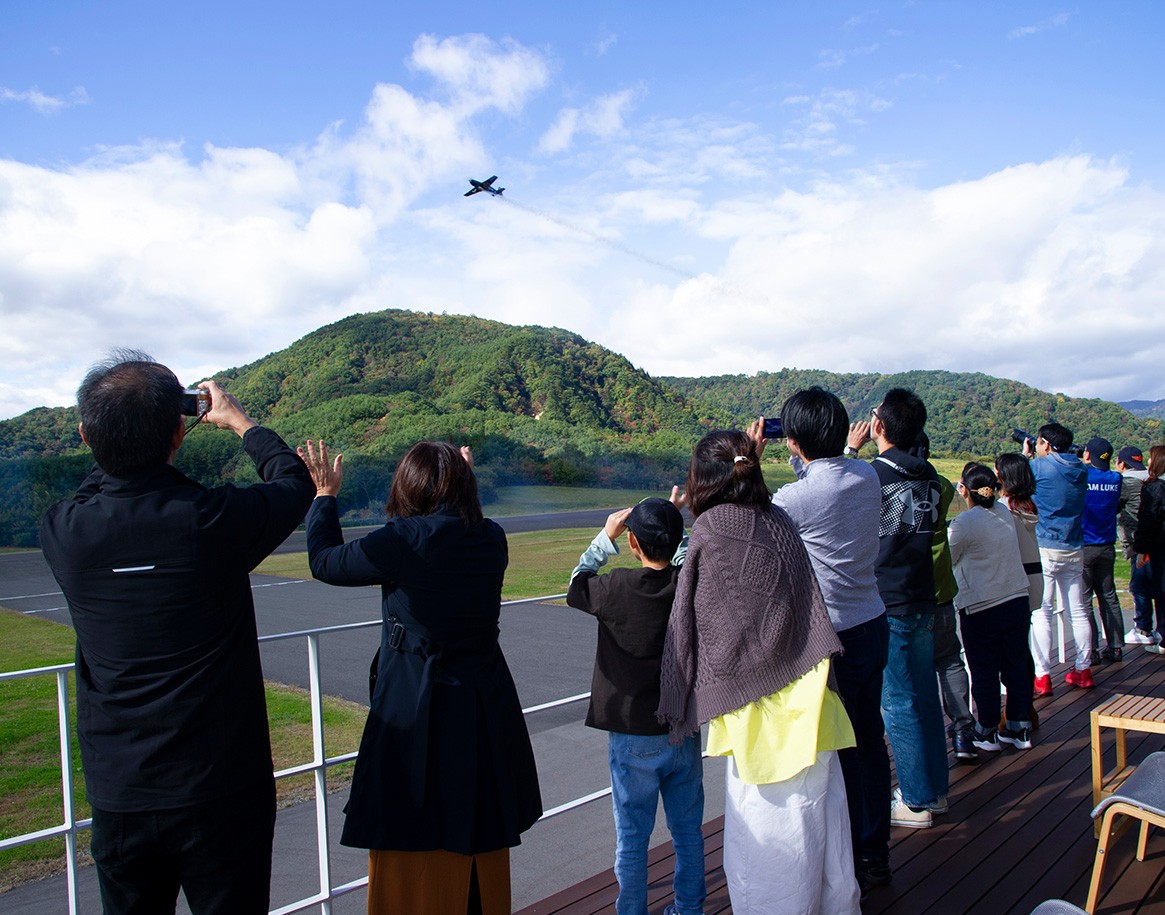 {generated} ゲストがクラブBreitlingチャレンジフライト2025の屋外航空イベントで丘上を旋回する航空機を見上げている