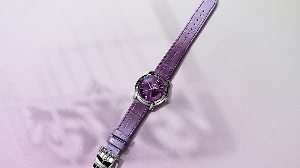 {generated} パープルのダイヤルとレザーストラップを備えたBreitling Lady Premierが柔らかなラベンダー背景に映える。