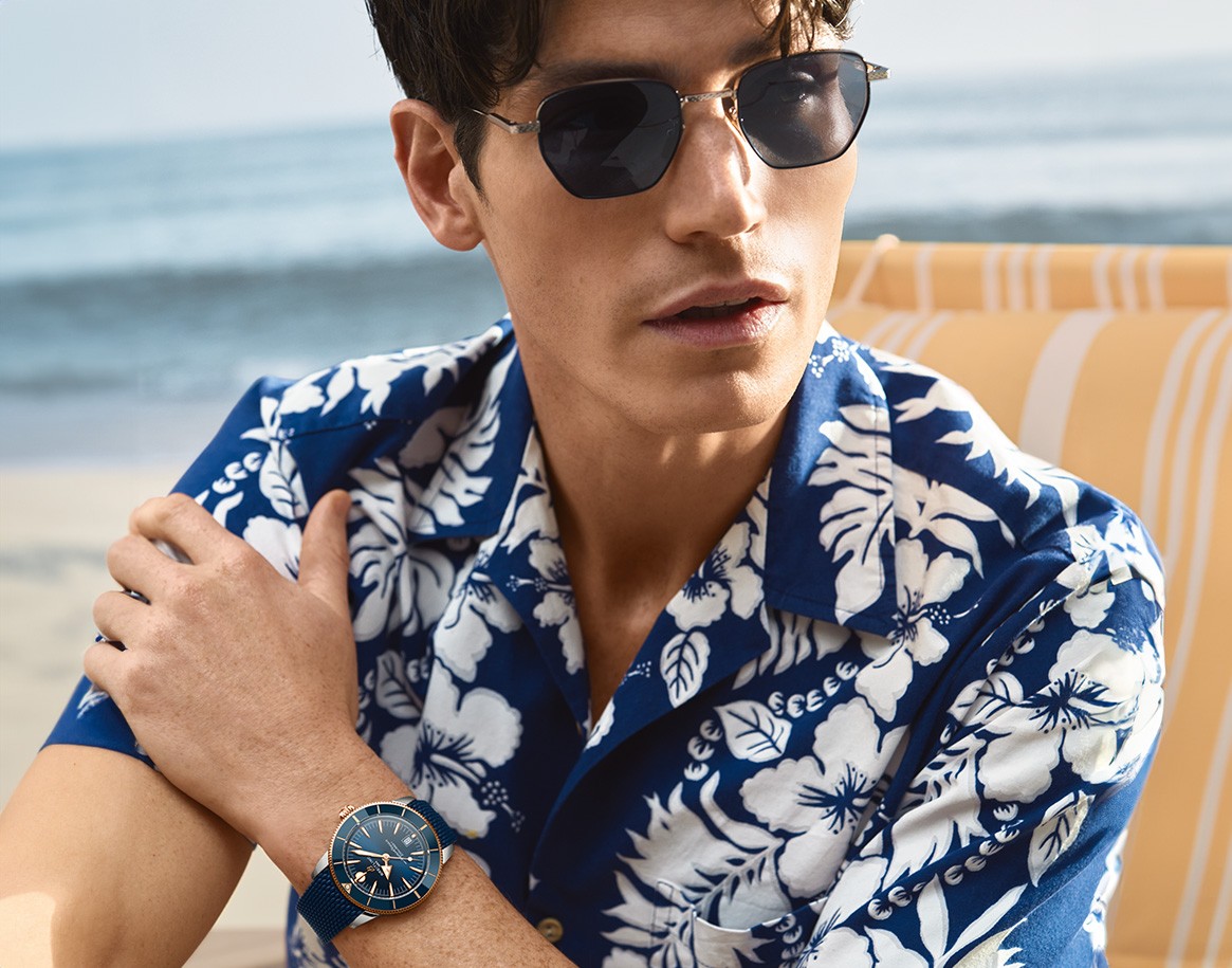 {generated} ビーチでサングラスを着用した男性が青いブレスレットのBreitling Superocean Heritageを身につけた夏のシーン