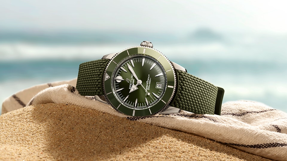 {generated} 海辺の砂上に置かれた緑の文字盤とストラップのBreitling Superocean Heritageで爽やかな夏の雰囲気を表現